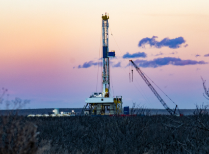 Fracking rig in a field with a purple sunset with clouds