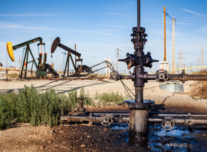 An oil pumpjack with a leaky wellhead is dripping with oil into a puddle along the side of a road