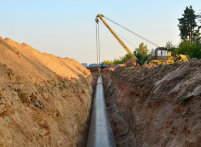 Crane bulldozer placing a natural gas pipeline in a dug trench in the ground.