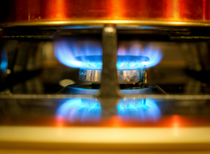 Gas stove burner ignited under a copper colored pot.